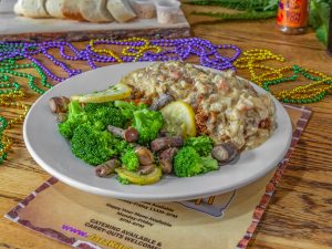 Jazz - A Louisiana Kitchen A plate of food featuring broccoli, mushrooms, and a creamy dish on a wooden table with colorful beads in the background. Kansas City, Columbia