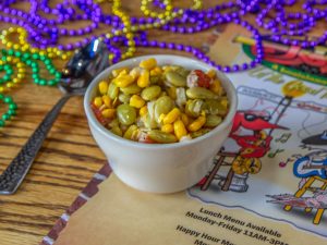 Jazz - A Louisiana Kitchen A bowl of corn and lima beans on a table with colorful beads, a spoon, and a decorative menu in the background. Kansas City, Columbia