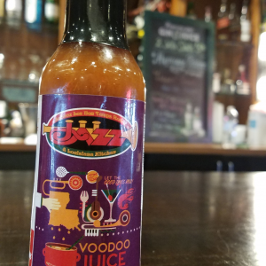 Jazz - A Louisiana Kitchen A bottle of Jazz Louisiana Kitchen Voodoo Juice hot sauce sits on a wooden table in a restaurant setting. Kansas City, Columbia, cajun food restaurant near me