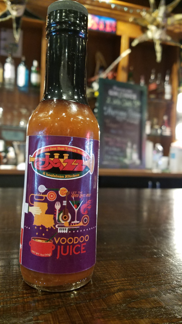 Jazz - A Louisiana Kitchen A bottle of Jazz Louisiana Kitchen Voodoo Juice hot sauce sits on a wooden table in a restaurant setting. Kansas City, Columbia, cajun food restaurant near me