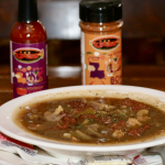 Jazz - A Louisiana Kitchen A bowl of gumbo is on a table, accompanied by a bottle of hot sauce and a seasoning shaker in the background. Napkins are placed beneath the bowl. Kansas City, Columbia, cajun food restaurant near me